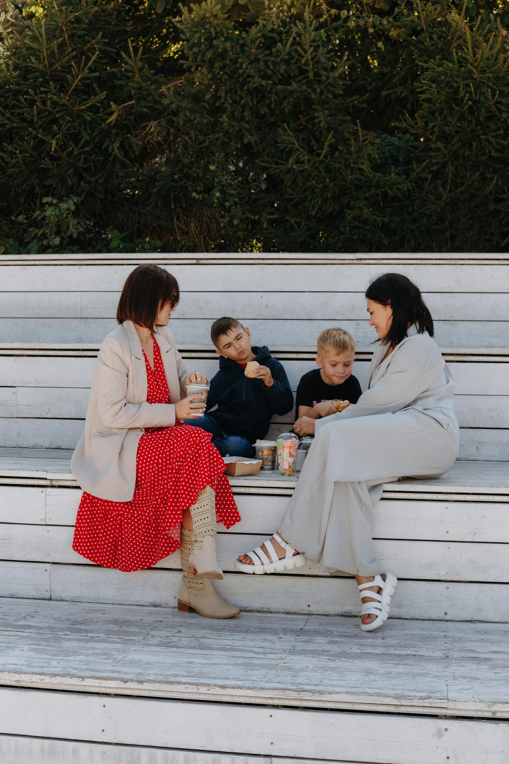 Two mothers and sons having lunch outdoors on sunny summer steps.